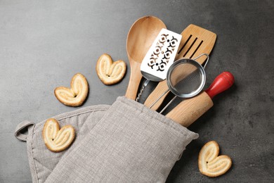 Photo of Different kitchen utensils in oven mitten and cookies on grey table, flat lay
