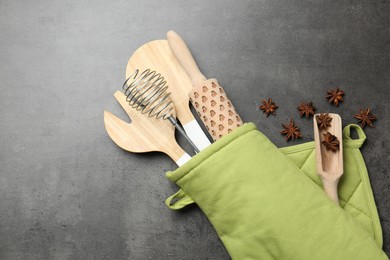 Photo of Different kitchen utensils in oven mitten and anise stars on grey table, flat lay