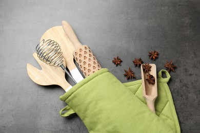 Photo of Different kitchen utensils in oven mitten and anise stars on grey table, flat lay