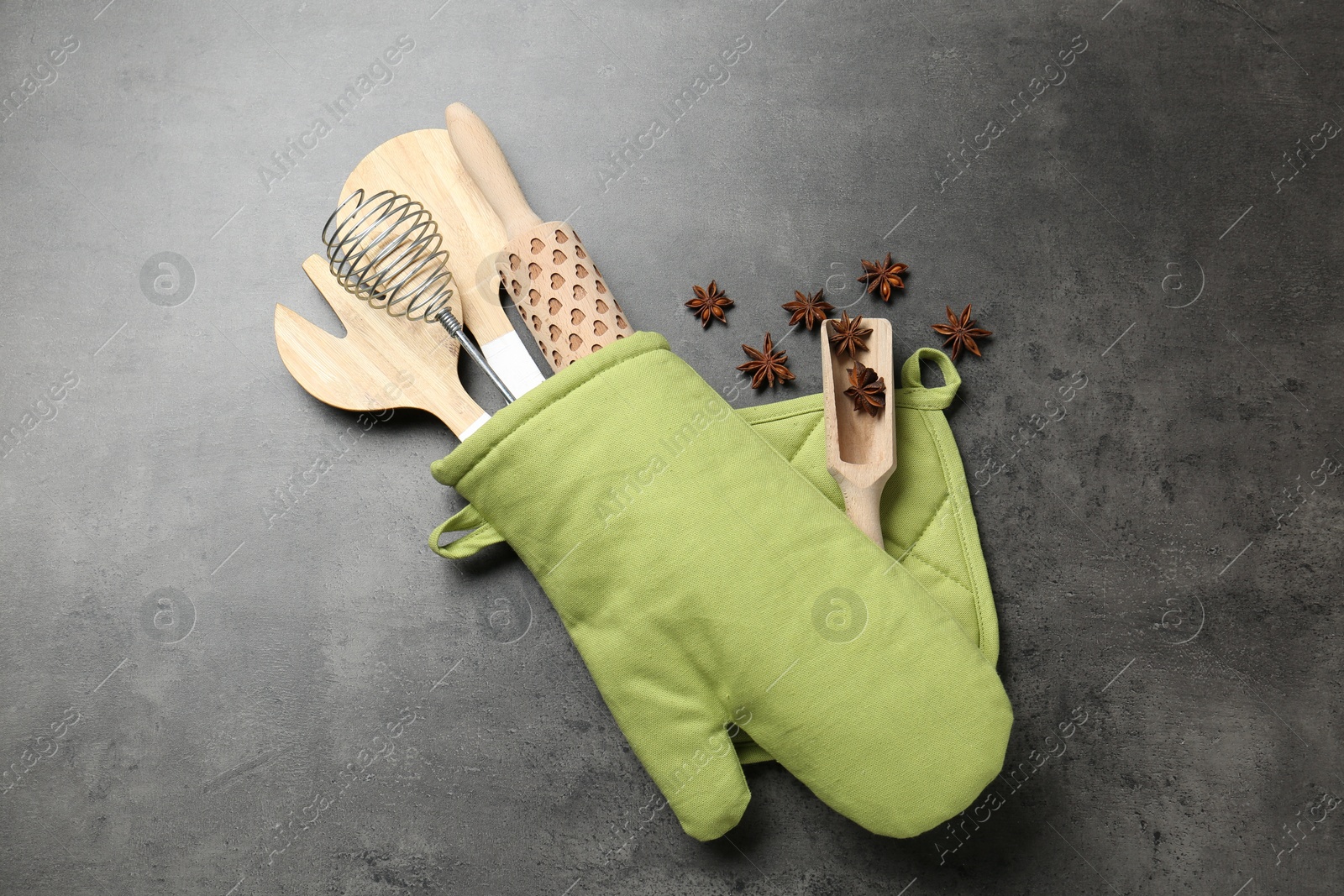 Different kitchen utensils in oven mitten and anise stars on grey table, flat lay Photo of Different kitchen utensils in oven mitten and anise stars on grey table, flat lay