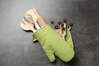 Photo of Different kitchen utensils in oven mitten and anise stars on grey table, flat lay