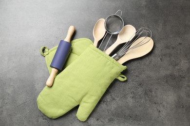 Photo of Different kitchen utensils in oven mitten on grey table, flat lay