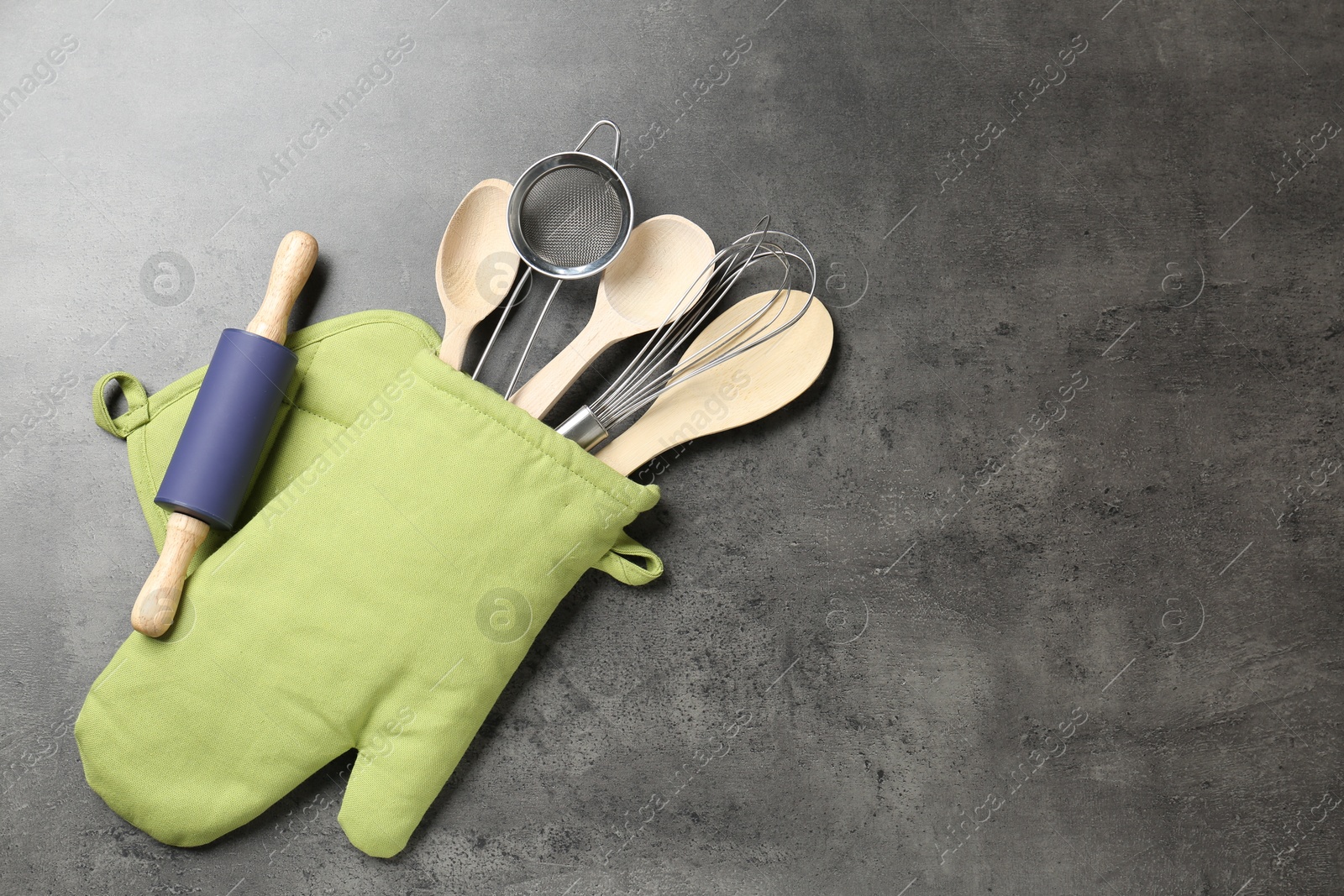 Different kitchen utensils in oven mitten on grey table, flat lay. Space for text Photo of Different kitchen utensils in oven mitten on grey table, flat lay. Space for text