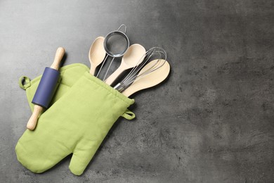 Photo of Different kitchen utensils in oven mitten on grey table, flat lay. Space for text