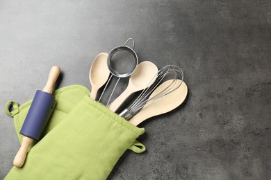 Photo of Different kitchen utensils in oven mitten on grey table, flat lay. Space for text