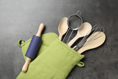 Photo of Different kitchen utensils in oven mitten on grey table, flat lay