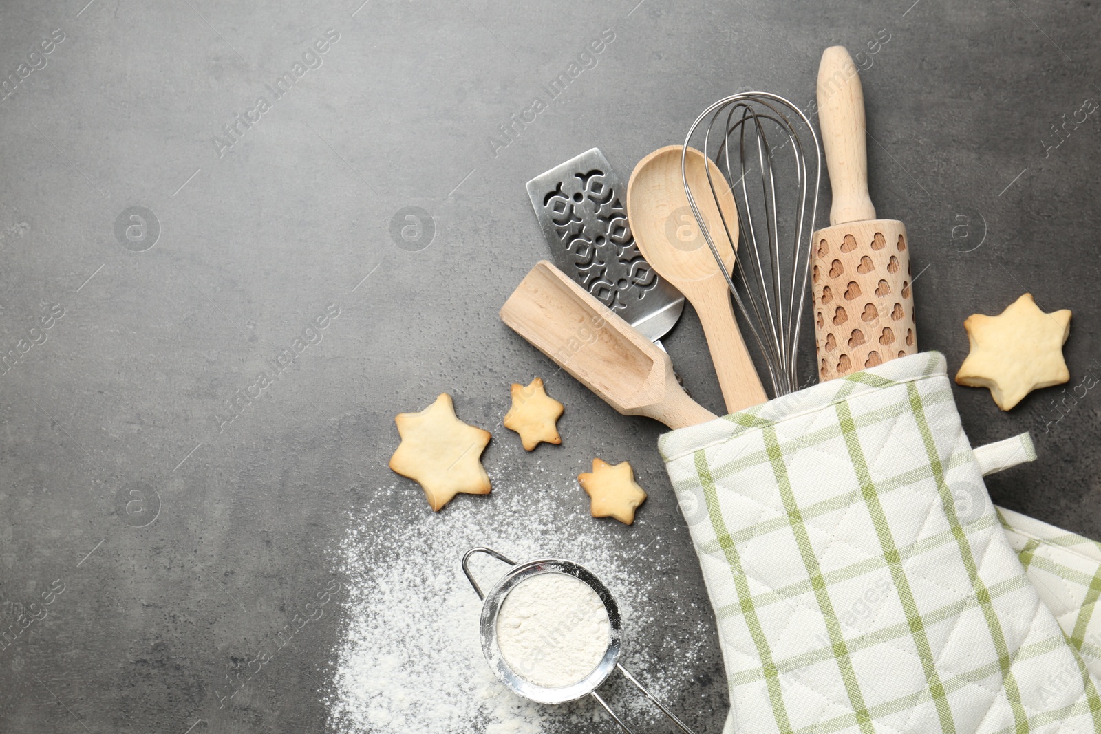 Different kitchen utensils in oven mitten, flour and cookies on grey table, flat lay. Space for text Photo of Different kitchen utensils in oven mitten, flour and cookies on grey table, flat lay. Space for text