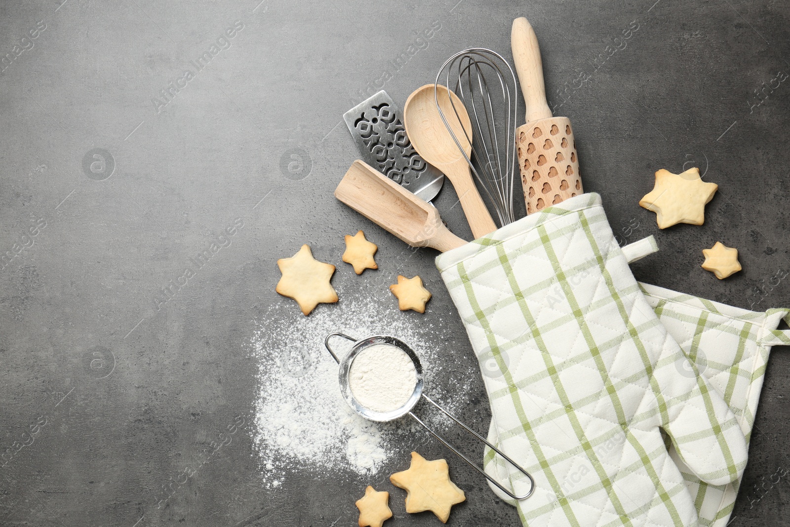 Different kitchen utensils in oven mitten, flour and cookies on grey table, flat lay. Space for text Photo of Different kitchen utensils in oven mitten, flour and cookies on grey table, flat lay. Space for text