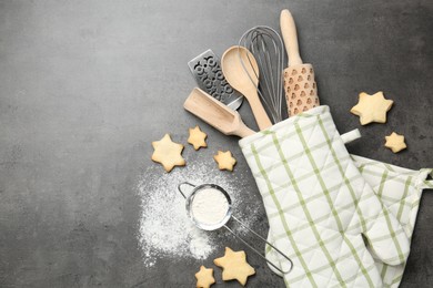 Photo of Different kitchen utensils in oven mitten, flour and cookies on grey table, flat lay. Space for text
