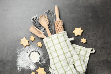 Photo of Different kitchen utensils in oven mitten, flour and cookies on grey table, flat lay