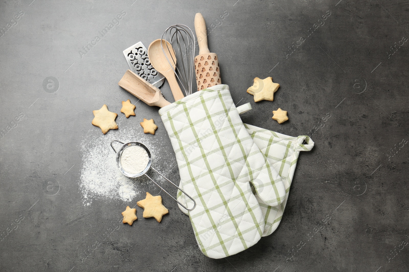 Different kitchen utensils in oven mitten, flour and cookies on grey table, flat lay Photo of Different kitchen utensils in oven mitten, flour and cookies on grey table, flat lay