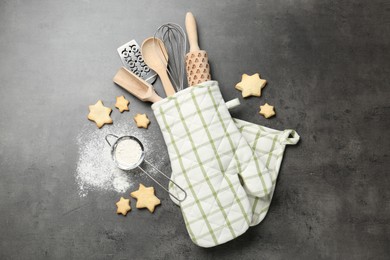Photo of Different kitchen utensils in oven mitten, flour and cookies on grey table, flat lay