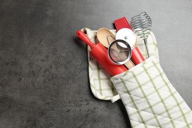 Photo of Different kitchen utensils in oven mitten on grey table, top view. Space for text