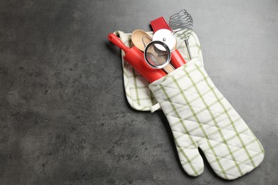 Photo of Different kitchen utensils in oven mitten on grey table, top view. Space for text