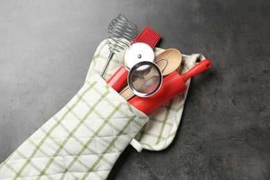 Photo of Different kitchen utensils in oven mitten on grey table, top view