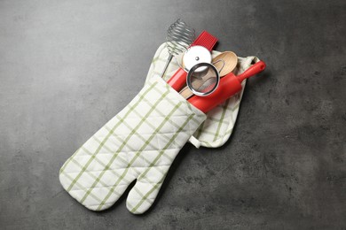 Photo of Different kitchen utensils in oven mitten on grey table, top view