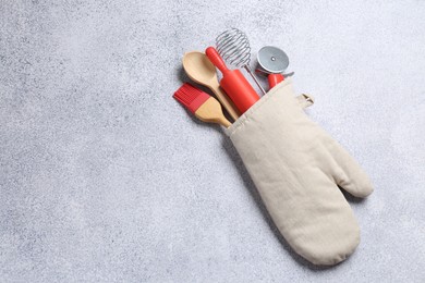 Photo of Different kitchen utensils in oven mitten on light table, top view. Space for text