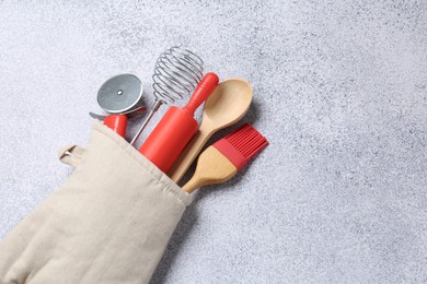 Photo of Different kitchen utensils in oven mitten on light table, above view. Space for text