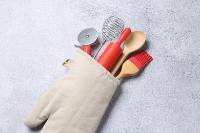 Photo of Different kitchen utensils in oven mitten on light table, above view