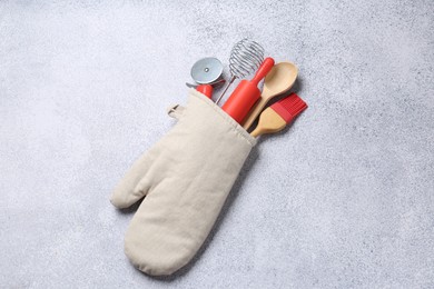 Photo of Different kitchen utensils in oven mitten on light table, top view