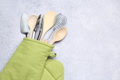 Photo of Different kitchen utensils in oven mitten on light table, top view. Space for text