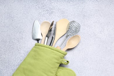 Photo of Different kitchen utensils in oven mitten on light table, top view