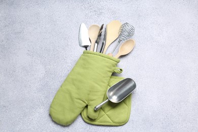 Photo of Different kitchen utensils in oven mitten on light table, top view