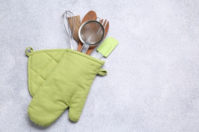 Photo of Different kitchen utensils in oven mitten on light table, top view. Space for text