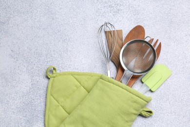 Photo of Different kitchen utensils in oven mitten on light table, top view. Space for text