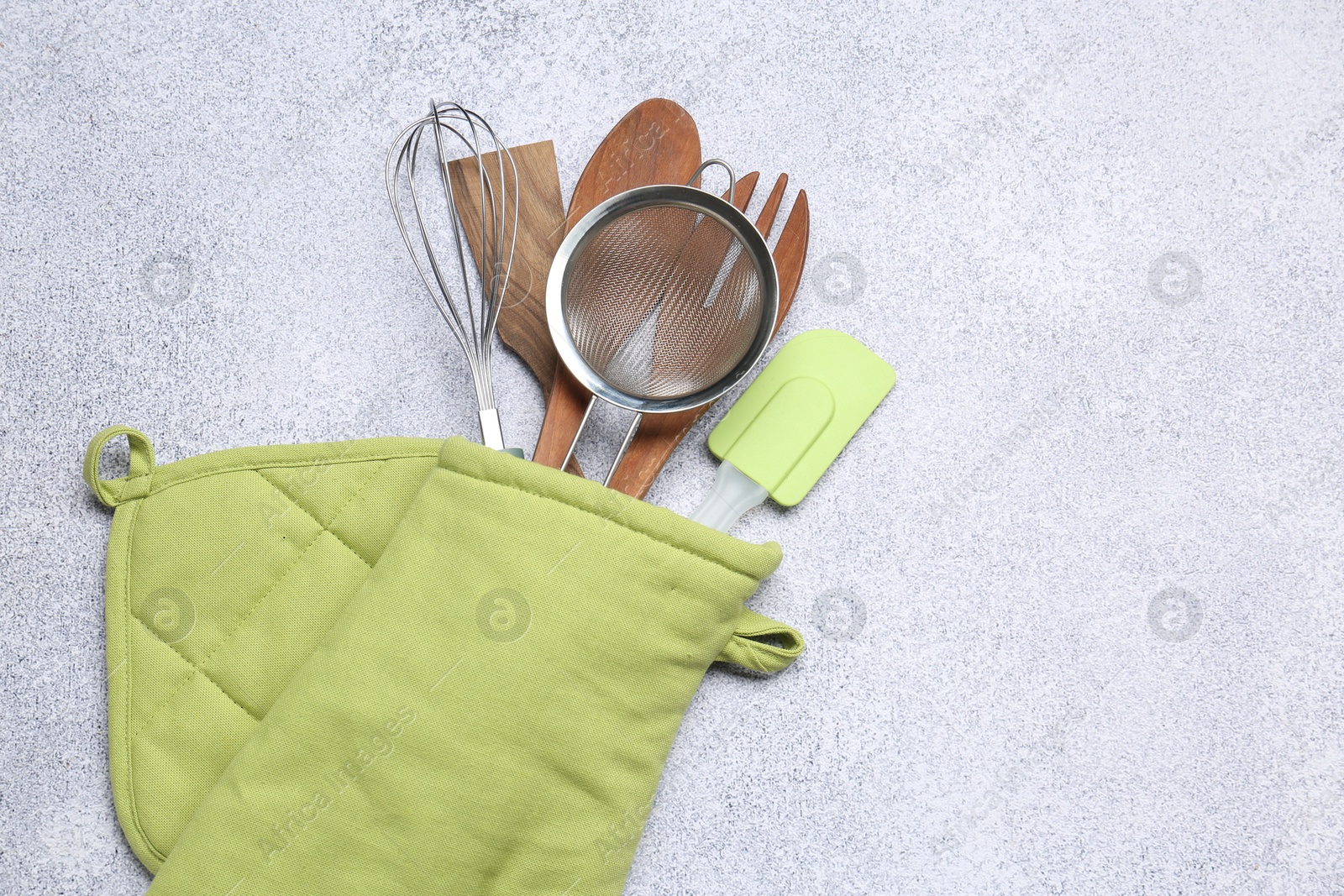 Different kitchen utensils in oven mitten on light table, top view. Space for text Photo of Different kitchen utensils in oven mitten on light table, top view. Space for text