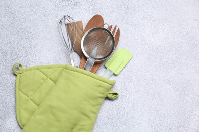 Photo of Different kitchen utensils in oven mitten on light table, top view. Space for text