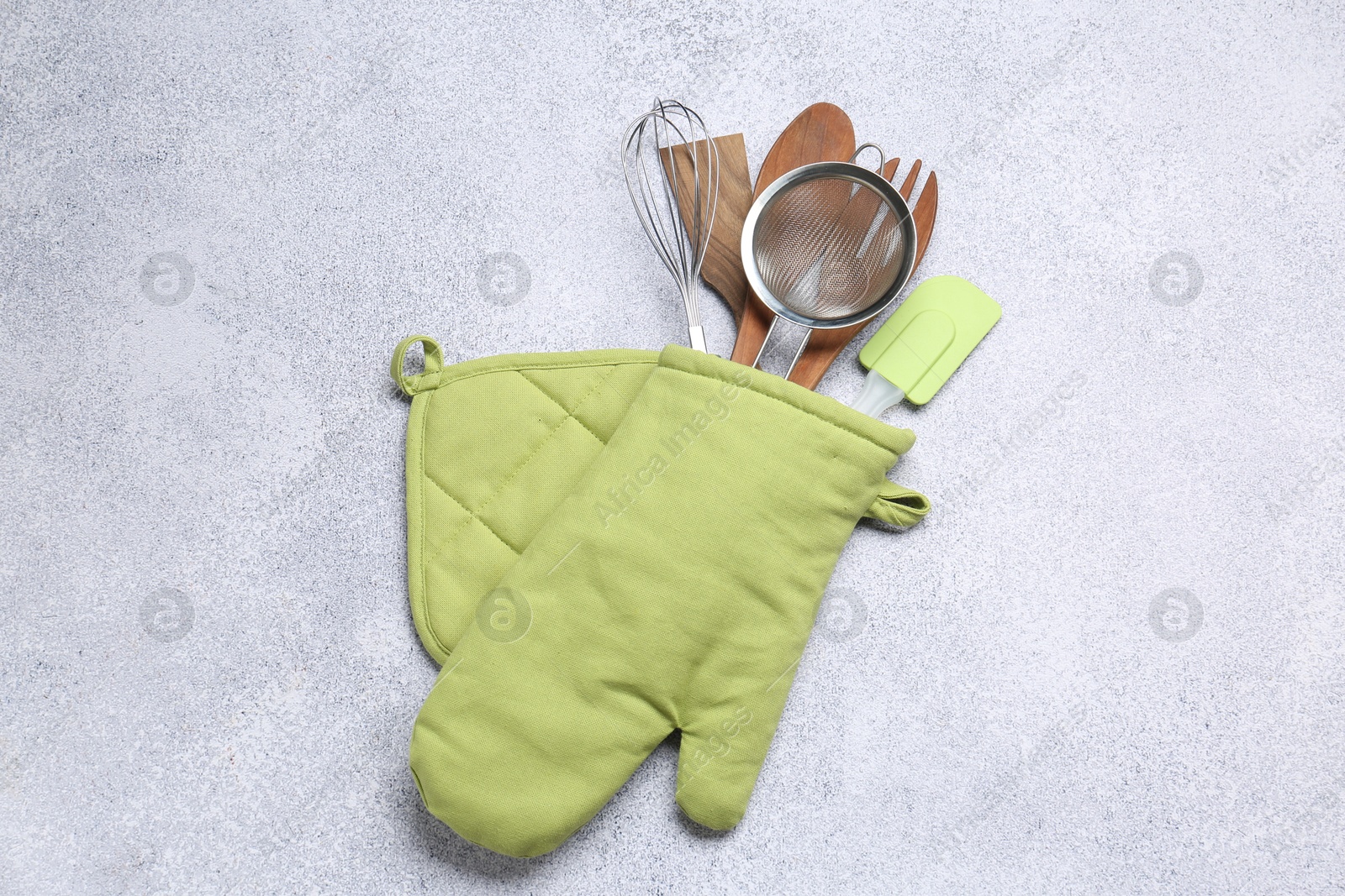 Different kitchen utensils in oven mitten on light table, top view Photo of Different kitchen utensils in oven mitten on light table, top view