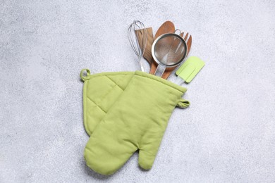 Photo of Different kitchen utensils in oven mitten on light table, top view