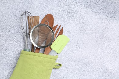 Photo of Different kitchen utensils in oven mitten on light table, top view. Space for text