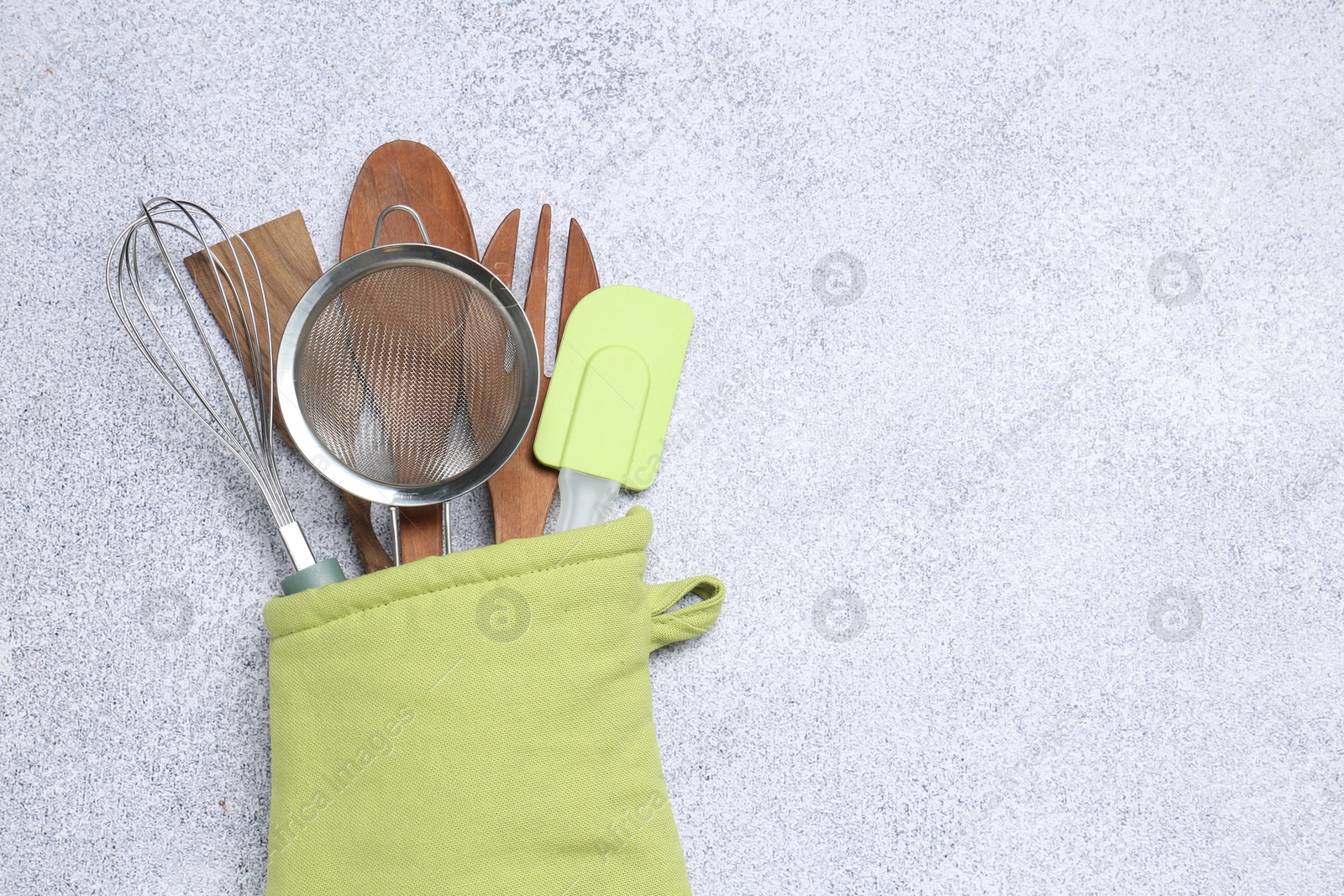 Different kitchen utensils in oven mitten on light table, top view. Space for text Photo of Different kitchen utensils in oven mitten on light table, top view. Space for text