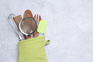 Photo of Different kitchen utensils in oven mitten on light table, top view. Space for text