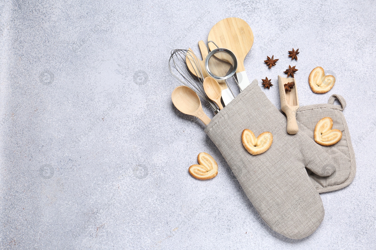 Different kitchen utensils in oven mitten, cookies and anise stars on light table, flat lay. Space for text Photo of Different kitchen utensils in oven mitten, cookies and anise stars on light table, flat lay. Space for text