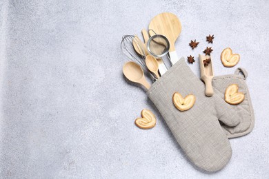 Photo of Different kitchen utensils in oven mitten, cookies and anise stars on light table, flat lay. Space for text