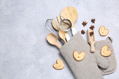Photo of Different kitchen utensils in oven mitten, cookies and anise stars on light table, flat lay. Space for text