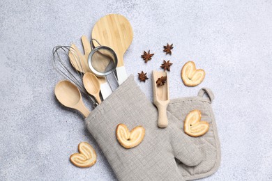 Photo of Different kitchen utensils in oven mitten, cookies and anise stars on light table, flat lay