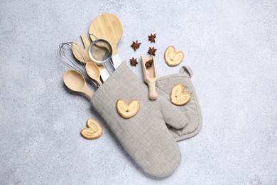 Photo of Different kitchen utensils in oven mitten, cookies and anise stars on light table, flat lay