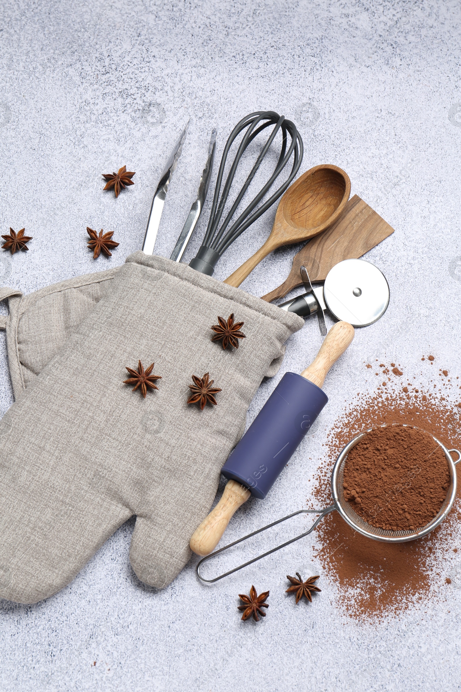 Different kitchen utensils in oven mitten, cocoa powder and anise stars on light table, flat lay Photo of Different kitchen utensils in oven mitten, cocoa powder and anise stars on light table, flat lay