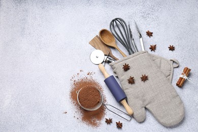 Photo of Different kitchen utensils in oven mitten, cocoa powder, cinnamon and anise stars on light table, flat lay. Space for text