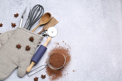 Photo of Different kitchen utensils in oven mitten, cocoa powder and anise stars on light table, flat lay. Space for text
