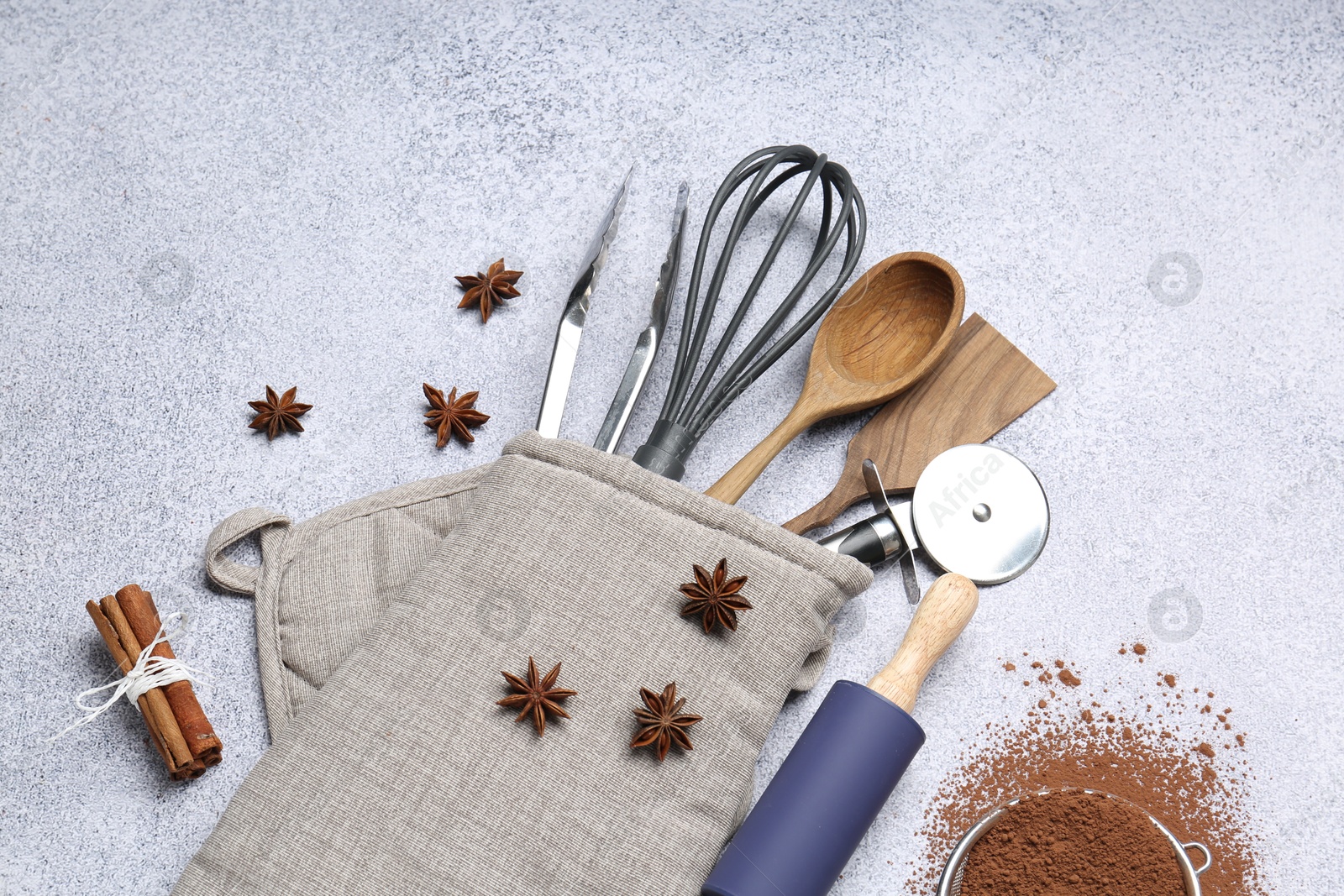 Different kitchen utensils in oven mitten, cocoa powder, cinnamon and anise stars on light table, flat lay Photo of Different kitchen utensils in oven mitten, cocoa powder, cinnamon and anise stars on light table, flat lay