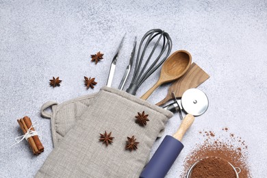Photo of Different kitchen utensils in oven mitten, cocoa powder, cinnamon and anise stars on light table, flat lay