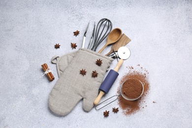 Photo of Different kitchen utensils in oven mitten, cocoa powder, cinnamon and anise stars on light table, flat lay