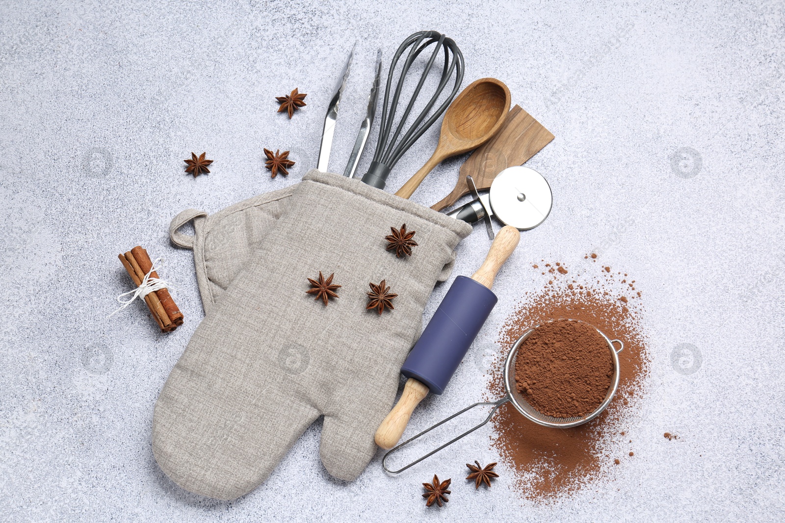 Different kitchen utensils in oven mitten, cocoa powder, cinnamon and anise stars on light table, flat lay Photo of Different kitchen utensils in oven mitten, cocoa powder, cinnamon and anise stars on light table, flat lay