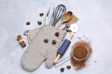 Photo of Different kitchen utensils in oven mitten, cocoa powder, cinnamon and anise stars on light table, flat lay