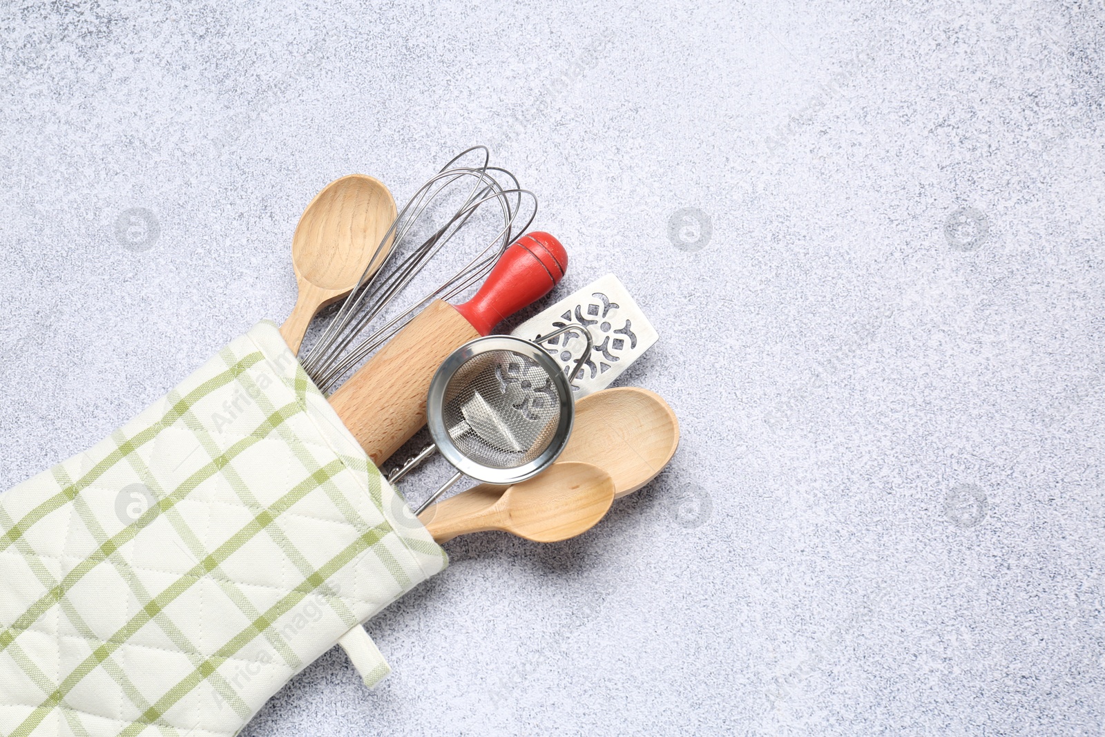 Different kitchen utensils in oven mitten on light table, top view. Space for text Photo of Different kitchen utensils in oven mitten on light table, top view. Space for text